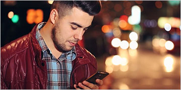Photograph of male student looking on phone: Go Mobile with the MindTap App